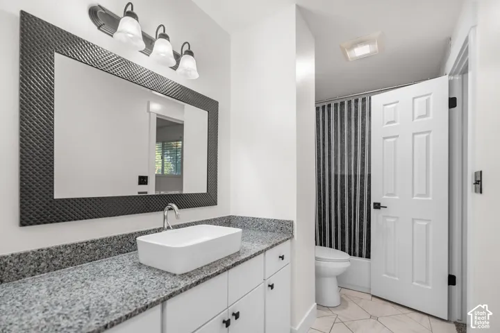 White vanity with a vessel sink, textured mirror, granite-finish countertop, brushed nickel faucet, and a shower with a privacy screen