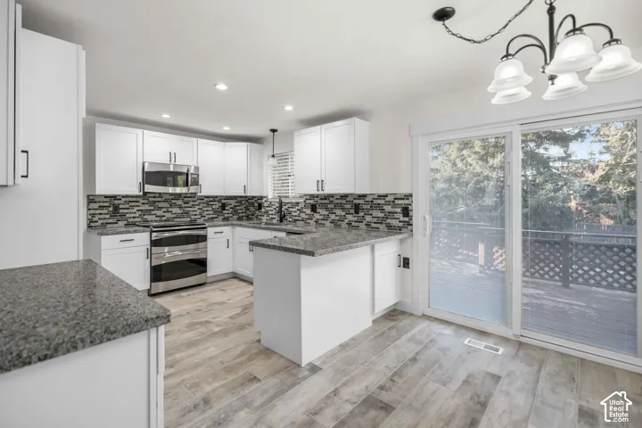White shaker cabinetry, stainless steel appliances, mosaic tile backsplash, wood-look flooring, and sliding glass door to exterior deck