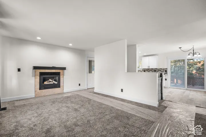 Fireplace with stone surround and black mantel, recessed lighting, gray carpeting, sliding glass door, and a built-in banister