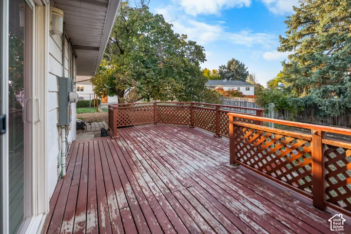 Expansive wood deck with lattice railing, bordered by mature trees and a sliding glass door entry
