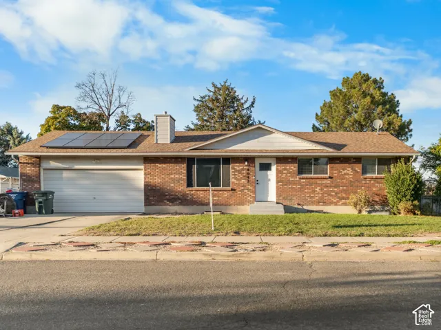 Brick exterior with white trim, attached two-car garage, asphalt shingle roof, and solar panels