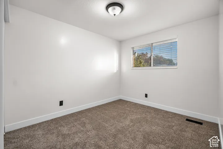 Recessed ceiling light fixture, window with horizontal blinds, and neutral carpet flooring