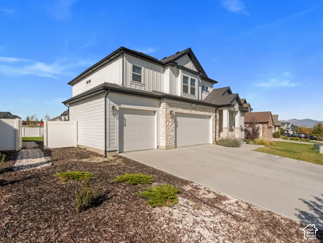 Contemporary exterior featuring white siding, stone accents, black-trimmed windows, and a multi-car garage with a concrete driveway