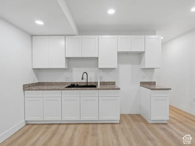 White shaker-style cabinetry, dark speckled countertops, black undermount sink, black gooseneck faucet, and wood-finish flooring