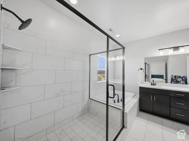 Walk-in shower with tile surround and built-in shelving, matte black rain showerhead, soaking tub, dark wood-finish vanity with countertop, and large mirror with overhead lighting