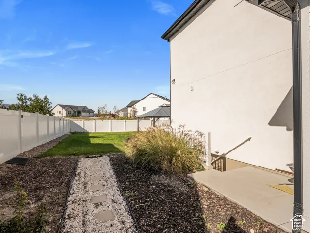Manicured lawn with mature landscaping, full perimeter fencing, concrete patio area, and stepping stone pathway