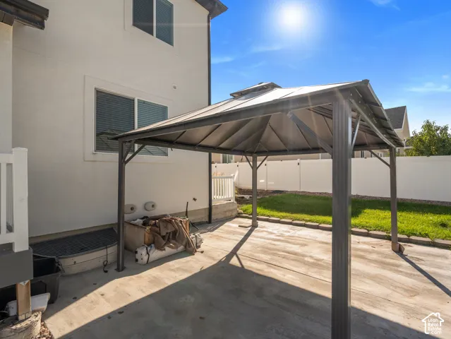 Concrete patio with a freestanding gazebo, complemented by a manicured lawn and white privacy fencing