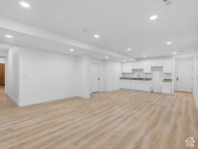 Spacious room featuring light wood-finish flooring, recessed lighting, and a built-in wet bar with white cabinetry, a single basin sink, and stone-finish countertops