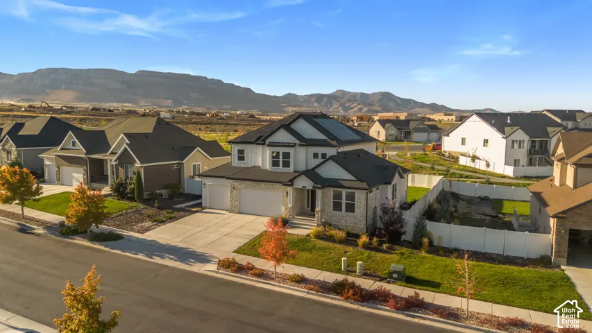 Modern two-story residence featuring white siding and stone accents, a multi-car garage, and a landscaped front yard with mature trees
