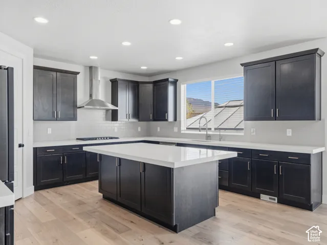 Contemporary kitchen featuring dark wood cabinetry, light-toned countertops, a central island, stainless steel range hood, and wood-finish flooring