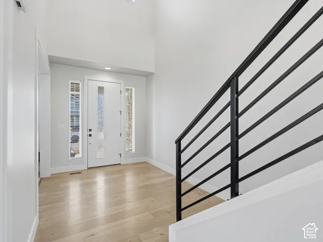 Two-story foyer with light wood-finish flooring, a white entry door with frosted glass, and black metal stair railing