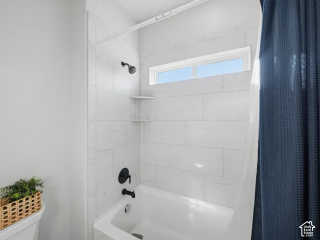 Bathtub with white subway tile surround, matte black fixtures, and built-in corner shelving