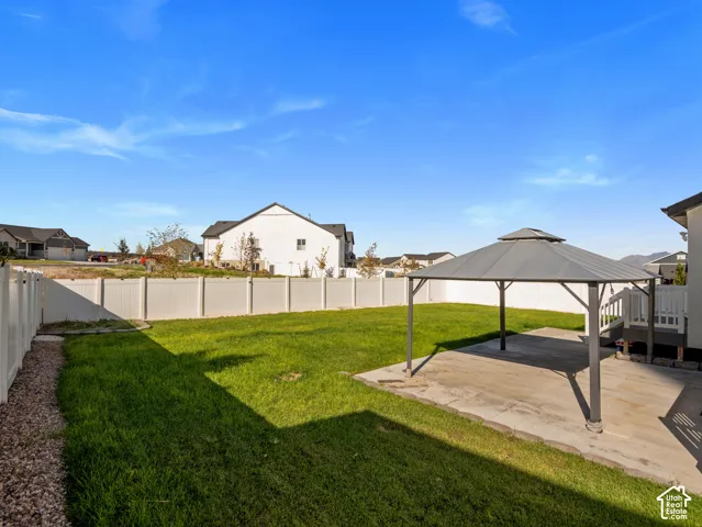 Expansive backyard featuring a concrete patio, a gazebo, a green lawn, and a white privacy fence