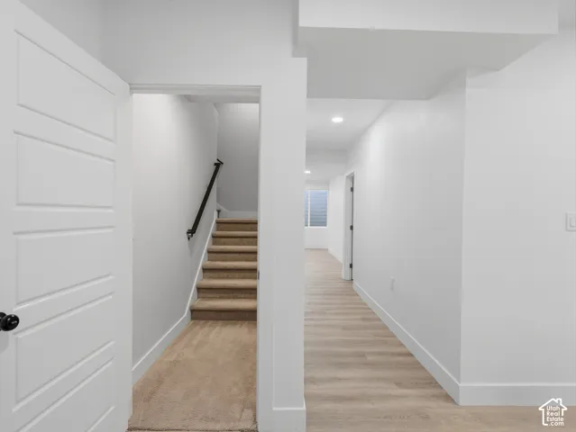 Modern interior door, carpeted staircase with black handrail, light wood-finish flooring, and recessed ceiling lighting