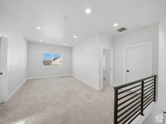 Recessed lighting, light-colored carpeting, white walls, and a modern black metal railing