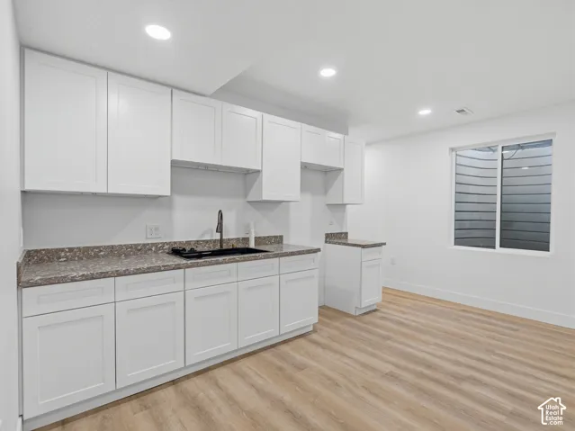 White shaker-style cabinetry, dark granite-finish countertops, black sink with a matte black faucet, recessed lighting, and wood-finish flooring
