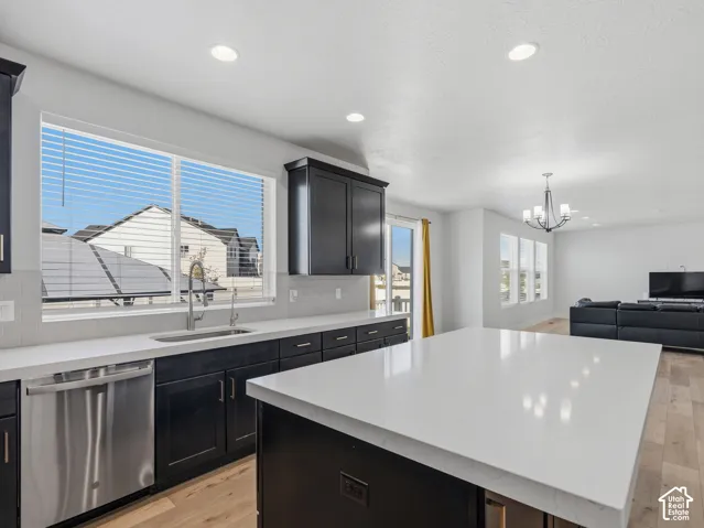 Kitchen featuring an expansive island with a light-colored countertop, dark wood-finish cabinetry, stainless steel dishwasher, and a window above the sink