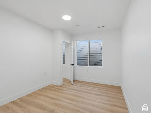 Recessed ceiling lighting, light wood-finish flooring, white walls, white trim, and a window with a window well