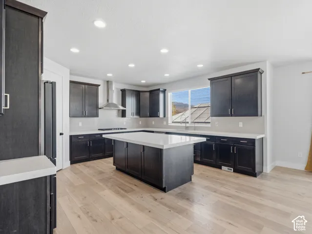 Kitchen featuring dark wood-finish cabinetry, light-toned countertops, a central island, and wood-finish flooring