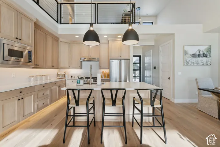 Open-concept kitchen featuring light wood-finish cabinetry, stainless steel appliances, a large center island with seating, and wood-finish flooring