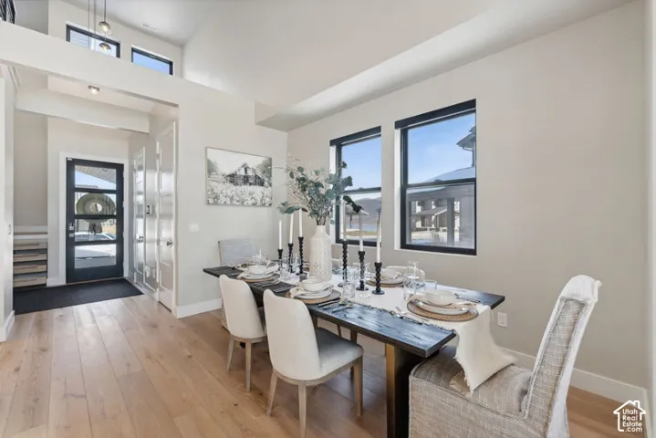 Bright dining space showcasing wood-finish flooring, abundant natural light from multiple large windows, and a black dining table with upholstered seating
