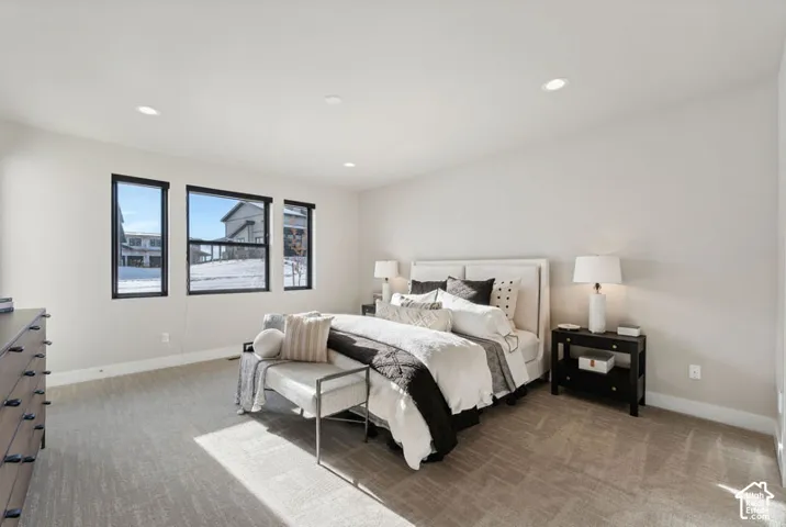 Recessed lighting, light-toned carpeting, multiple windows with dark framing, and neutral wall tones
