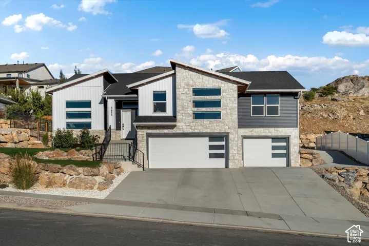 Contemporary exterior with stone and vertical siding accents, dual garage doors with modern window inserts, concrete driveway, and tiered rock landscaping