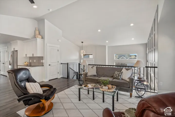 Vaulted ceilings with recessed lighting, wood-finish flooring, white cabinetry with stainless steel appliances, and a wrought iron railing system