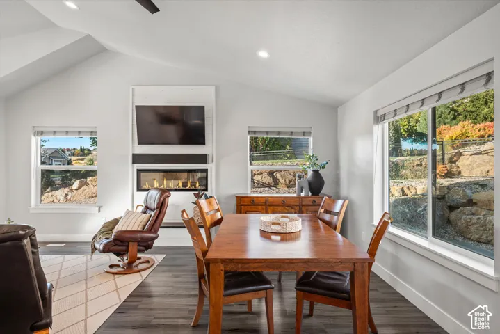 Vaulted ceiling with recessed lighting, linear electric fireplace, wood-finish flooring, multiple windows, and exterior rock landscaping