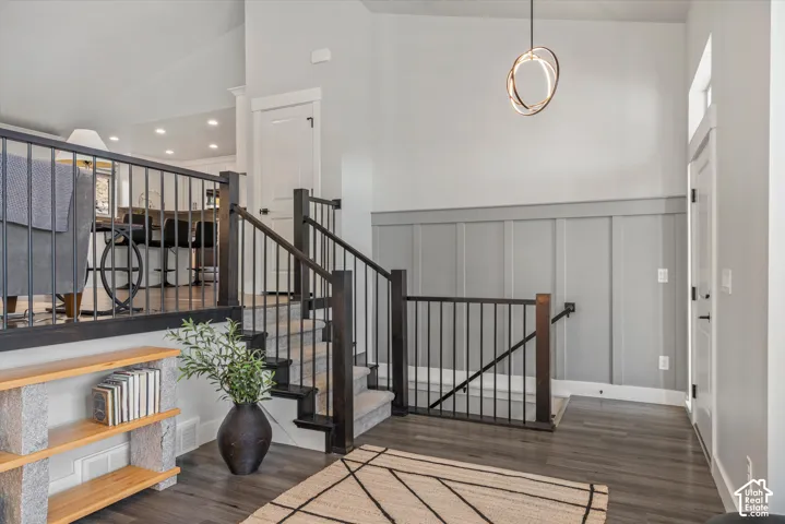 Vaulted ceiling with a contemporary pendant light fixture, board and batten accent wall, wood-finish flooring, and a two-tone staircase with black metal balusters