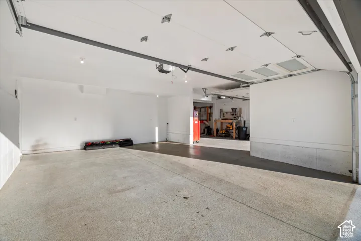 Garage with concrete flooring, exposed overhead door mechanism, recessed lighting, and a partial view into an additional space