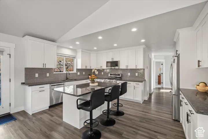 Kitchen featuring white shaker cabinetry, dark countertops, a mosaic tile backsplash, stainless steel appliances, and wood-finish flooring
