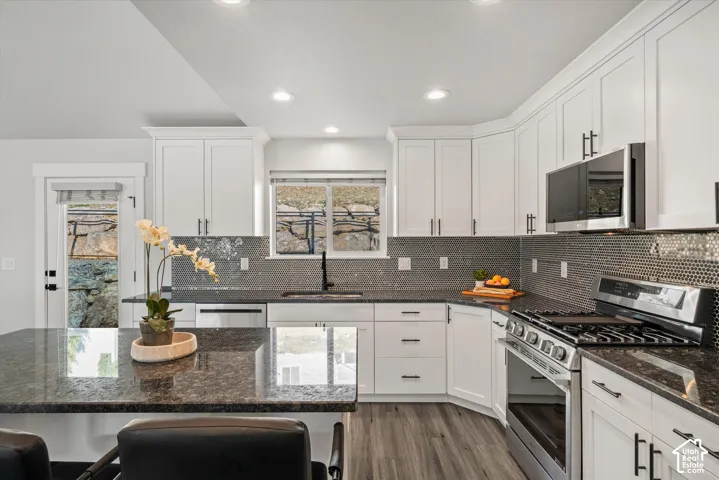 Kitchen featuring white shaker cabinetry, dark granite countertops, stainless steel appliances, a mosaic tile backsplash, and wood-finish flooring