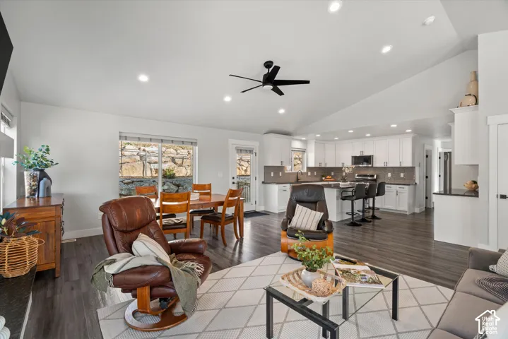 Vaulted ceiling with recessed lighting, wood-finish flooring, white cabinetry, dark countertops, and a kitchen island with bar seating
