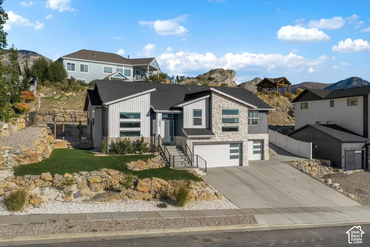 Modern exterior with stone accents and vertical siding, featuring a dual garage, concrete driveway, and landscaped rock retaining walls