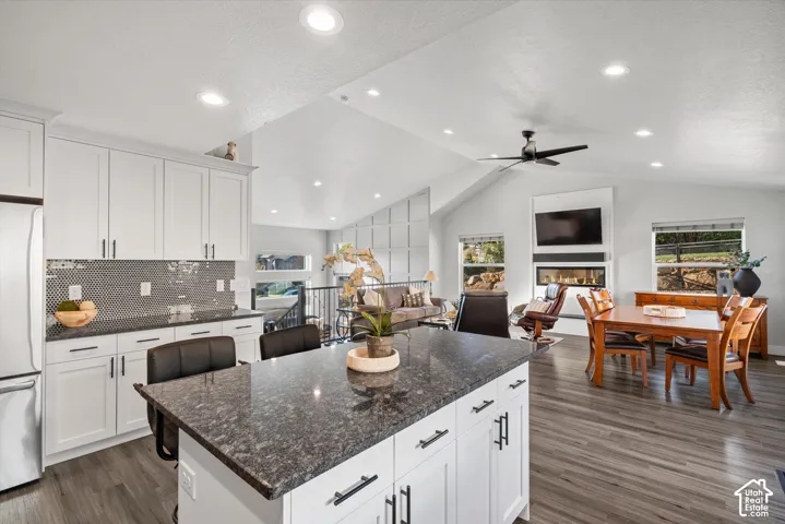 Vaulted ceiling, recessed lighting, wood-finish flooring, white cabinetry, and a built-in fireplace