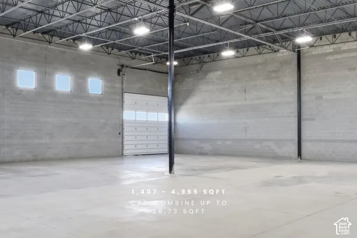 Concrete block walls, exposed metal ceiling trusses, polished concrete flooring, multiple square windows, and a large roll-up door