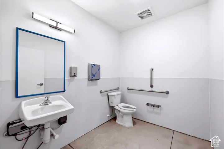 Wall-mounted sink with single-handle faucet, rectangular mirror with blue frame, and white toilet with support bars