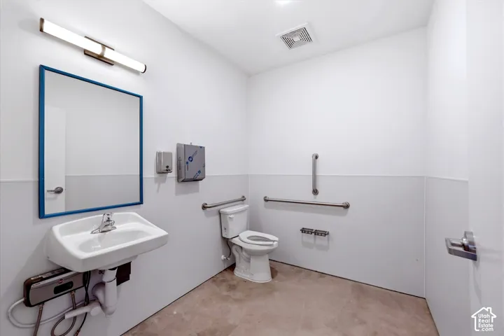 White wall paneling with a wall-mounted sink, a toilet, and stainless steel grab bars