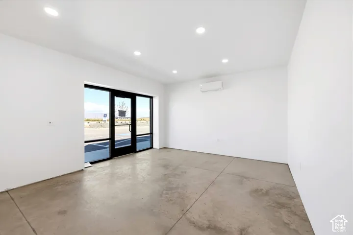 Recessed ceiling lighting, concrete flooring, sliding glass door entry, split air conditioning unit, and white painted walls