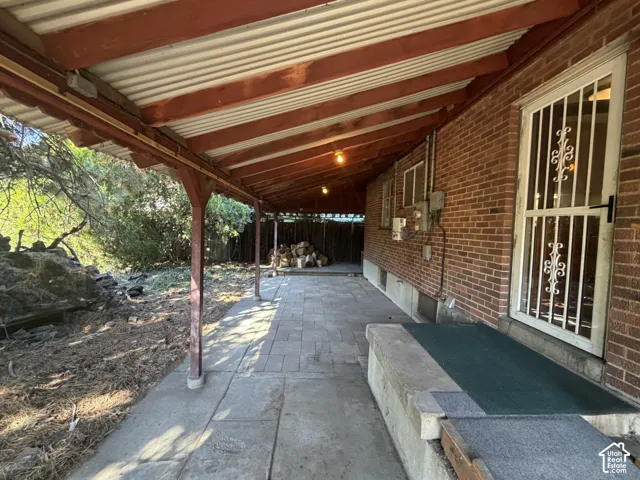 Covered patio with a corrugated roof, brick exterior, and a stone paver and concrete walkway