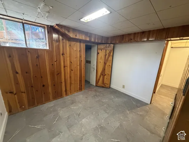 Wood-paneled wall, window, gray tile flooring, white walls, and a wood barn door