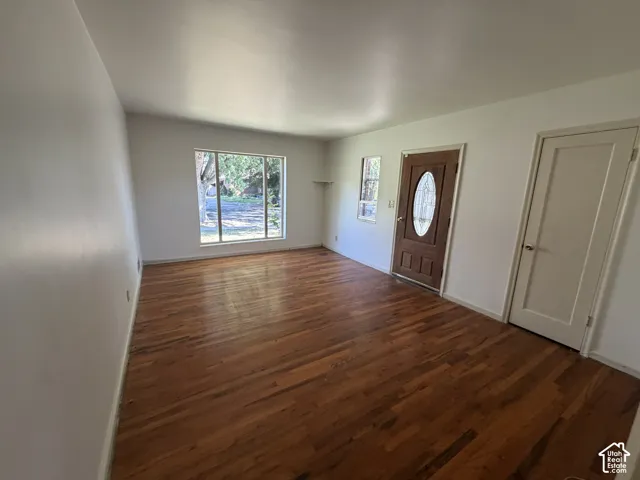 Hardwood flooring, front door with oval glass insert, large picture window, white painted walls, and a flat-panel interior door