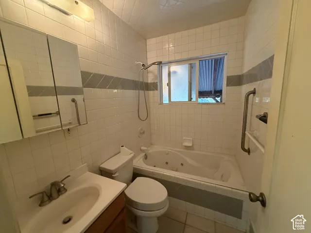 Bathroom featuring a jetted tub, tiled shower surround with accent band, vanity with integrated sink, and wall-mounted grab bars
