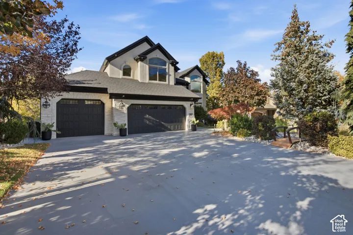 Multi-level exterior featuring light-toned masonry, dark-toned garage doors, asphalt shingle roofing, and an expansive concrete driveway