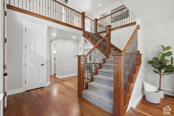 Grand foyer featuring wood-finish flooring, a staircase with decorative metal balusters and natural wood railings, and recessed lighting