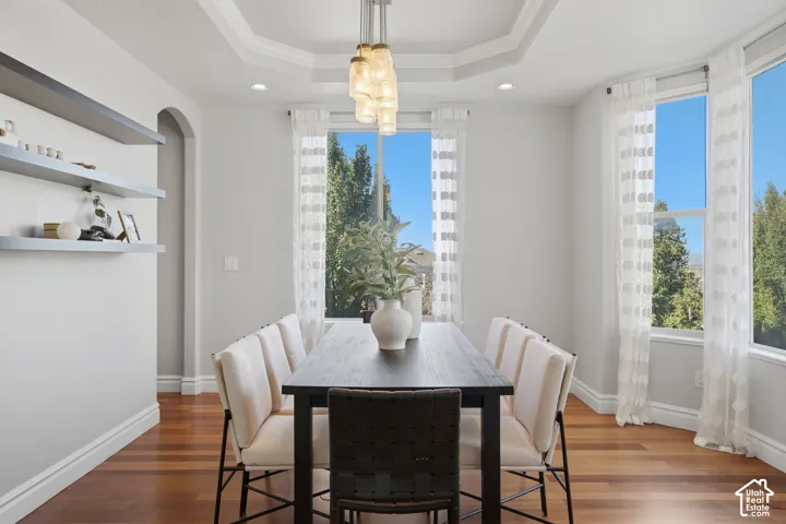 Dining space featuring a tray ceiling, wood-finish flooring, built-in shelving, arched architectural detail, and multi-light hanging fixture