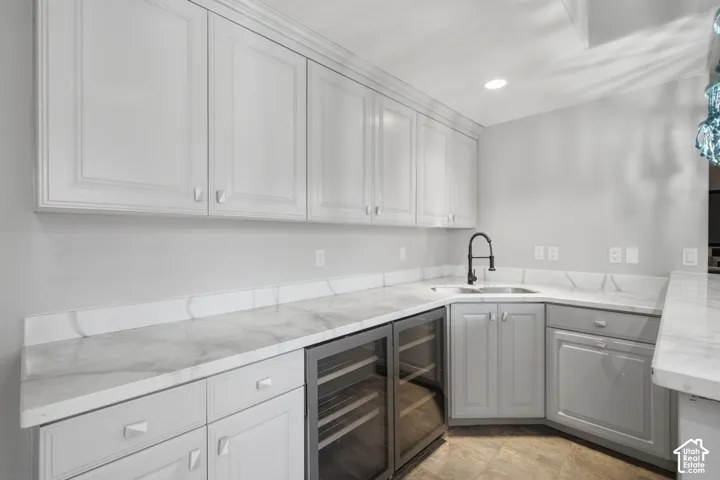 Custom cabinetry with shaker-style detailing, stone-surface countertops, full-height tile backsplash, stainless steel under-mount sink with matte black gooseneck faucet, and dual built-in glass-front beverage refrigerators