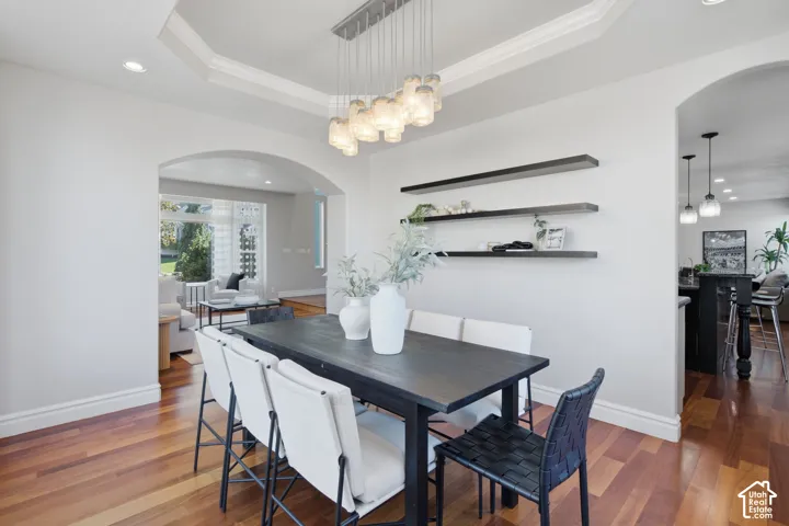 Tray ceiling featuring recessed lighting, multi-pendant light fixture, wood-finish flooring, and built-in wall shelving