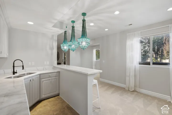 Custom kitchen area featuring a stone-surface peninsula, gray cabinetry, a dual-basin sink with a matte black faucet, and three decorative pendant lights